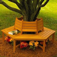 a wooden bench sitting under a tree on top of a grass covered park area with flowers around it