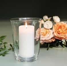 a white candle sitting next to a glass vase with flowers in it on a table