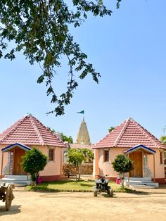 two small pink houses sitting in the middle of a dirt field next to a tree