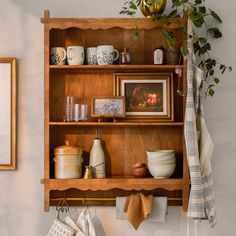 a wooden shelf filled with dishes and other items next to a potted plant on top of a table