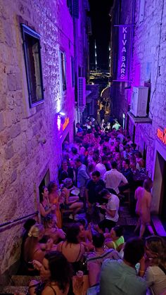 a group of people sitting on the ground in an alleyway with purple lights at night