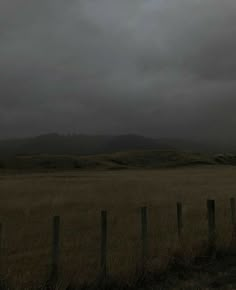 an empty field with a fence in the foreground and mountains in the distance under a cloudy sky