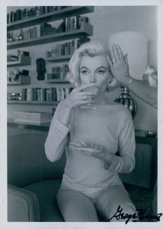 black and white photograph of woman drinking from glass in living room with bookshelves