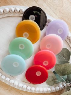 several different colored discs sitting on top of a white tray next to a green plant