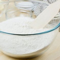 a bowl filled with white flour next to a wooden spoon on top of a table