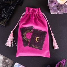 a pink bag with two tarot cards on it next to purple crystals and other items