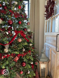 a decorated christmas tree in front of a window with red ribbon and ornaments on it