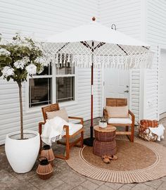 an outdoor patio area with wicker furniture and white umbrella on the side of the house