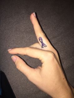 a person's hand with a purple ribbon tattoo on their left thumb and finger