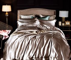 a bed with silver sheets and pillows in a room next to a lamp on a table