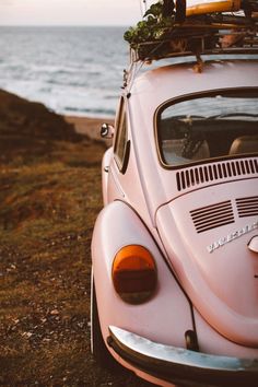 a pink vw beetle parked next to the ocean