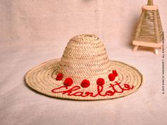 a straw hat with red pom poms on it next to a toy tree