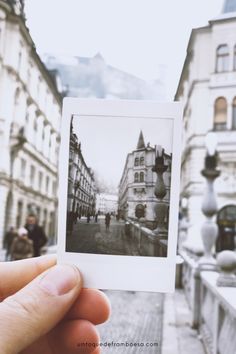 a hand holding up an old photo in front of buildings