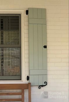 a wooden bench sitting in front of a window next to a white brick building with green shutters