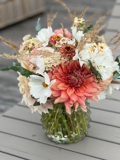 a vase filled with lots of flowers sitting on top of a wooden table covered in grass