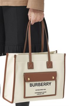 Pre-order this style today! Add to Shopping Bag to view approximate ship date. You'll be charged only when your item ships.Burberry's London headquarters address is stamped on the front pocket of this cotton canvas tote crafted with topstitched leather trim and hand-painted edges. Snap-tab closure Shoulder straps Exterior magnetic-flap pocket Interior zip and wall pockets Protective leather feet Cotton-and-linen canvas lining Textile with leather trim Made in Italy Designer Handbags Burberry Tote Bag, Burberry Tote, Canvas Leather Tote, Tan Woman, Burberry London, Printed Canvas, Natural Tan, Burberry Women, Burberry Bag