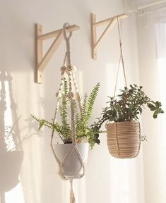 two hanging planters with plants in them on a white wall next to a window