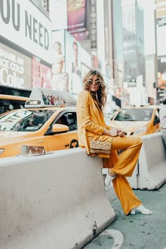 a woman sitting on the side of a wall next to taxi cabs in new york city