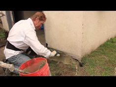 a man in white shirt and blue jeans working on cement wall next to red bucket