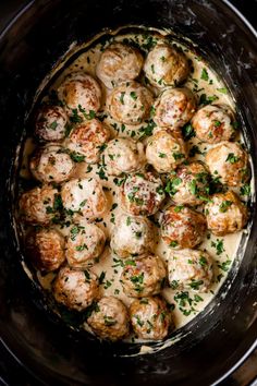 a crock pot filled with meatballs covered in gravy and garnished with parsley