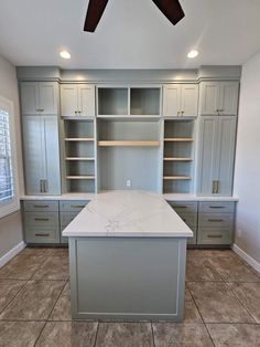 an empty kitchen with gray cabinets and white counter tops, two ceiling fans above the island