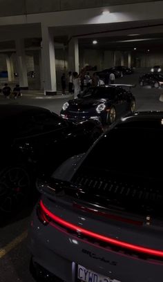 several cars parked in a parking garage with people standing around them and one car has its tail lights on