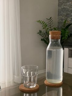 a glass and bottle sitting on top of a table next to a vase with a cork in it