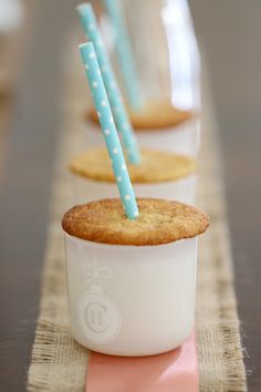 three cupcakes with blue and white straws in them sitting on a table