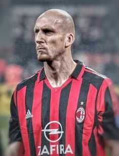 a soccer player in black and red uniform standing on the field with his head turned to the side