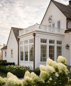 a white house with lots of windows and flowers in the foreground, on a sunny day