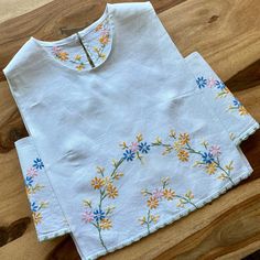 two white t - shirts with colorful flowers on them sitting on a wooden table next to a pair of scissors