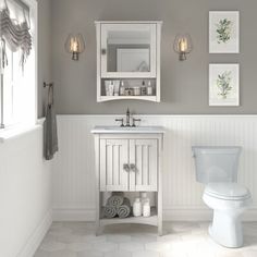 a white toilet sitting next to a sink in a bathroom under two pictures on the wall