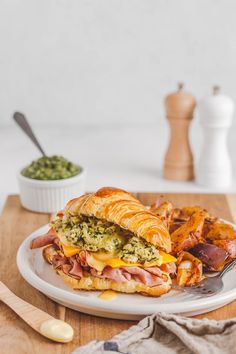 a sandwich and some potato chips on a plate next to a bowl of pesto