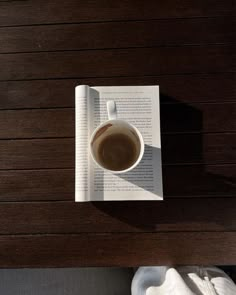 a cup of coffee sitting on top of a wooden table next to an open book