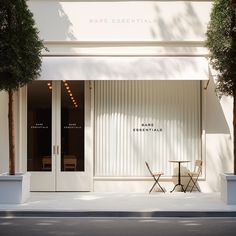 an empty table and two chairs in front of a white building with glass doors that say bare essential