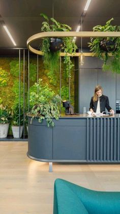 a woman sitting at a desk in front of a green wall with plants on it