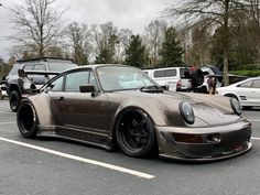 a silver porsche parked in a parking lot next to other cars and people standing around