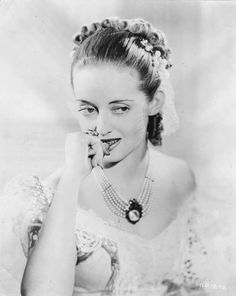 an old black and white photo of a woman with pearls on her head, smiling at the camera