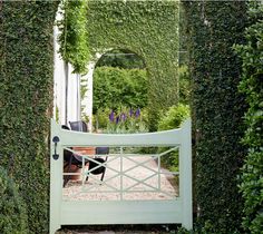 a white gate surrounded by greenery in the middle of a garden