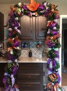 a kitchen decorated for halloween with purple and green decorations on the counter top, and an orange wreath hanging over the sink