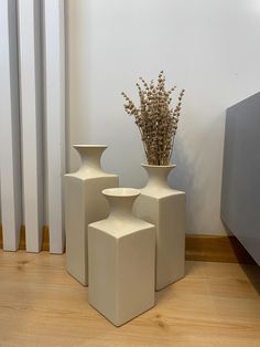 three white vases sitting next to each other on a wooden floor in front of a radiator