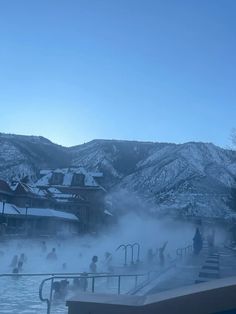 people are swimming in the hot tubs on a cold winter day with mountains in the background