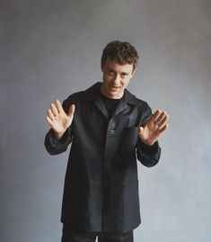 a man standing in front of a gray background holding his hands out to the side