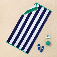 a blue and white striped towel sitting on top of a sandy beach next to shoes