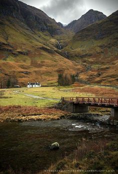 a bridge over a small stream in the middle of a field with mountains behind it