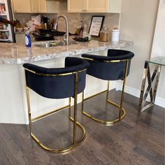 two blue velvet bar stools sitting in front of a marble counter top with gold legs