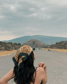 a woman sitting in the middle of an empty parking lot with mountains in the background