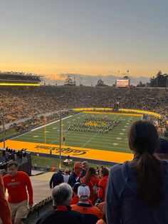 a football stadium filled with people watching the sun go down in the distance and there is a band playing on the field