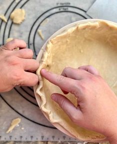 two hands are placing dough into a pie pan