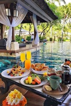 a table with food and drinks on it next to a pool in the middle of a resort